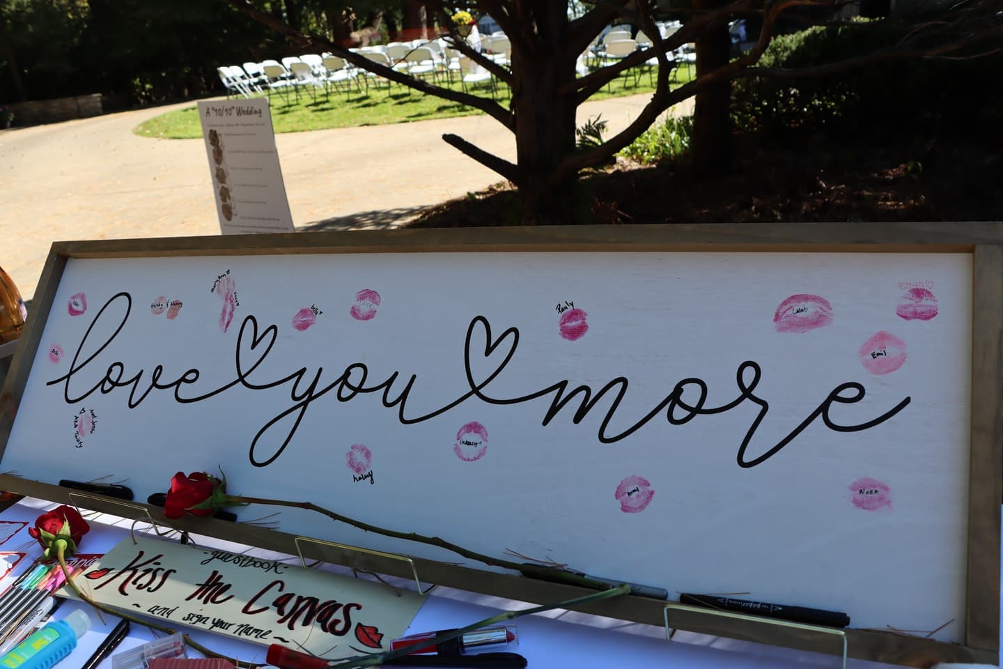 A white sign reading love you more, covered in lipstick kisses from guests