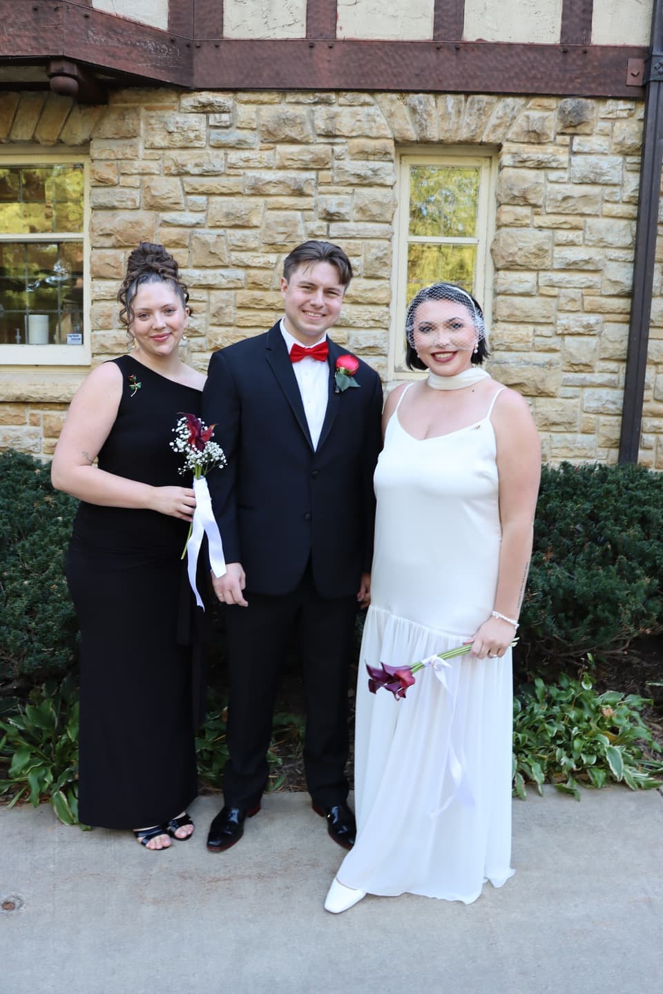 Abbi and Fred standing with a guest in a black dress outside the house