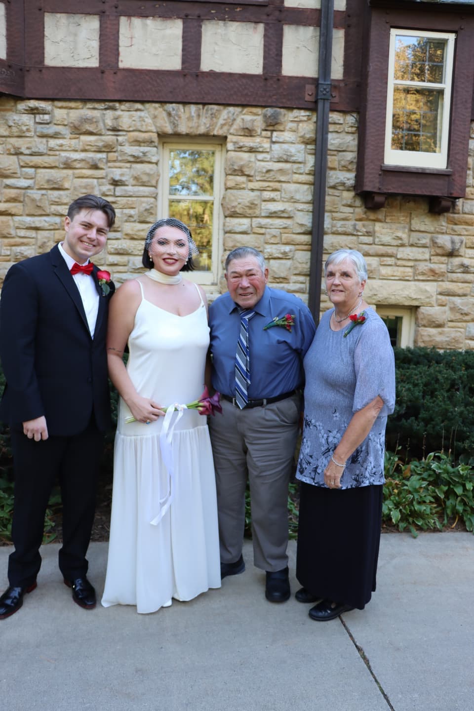 Abbi and Fred with two older family members in front of the stone house