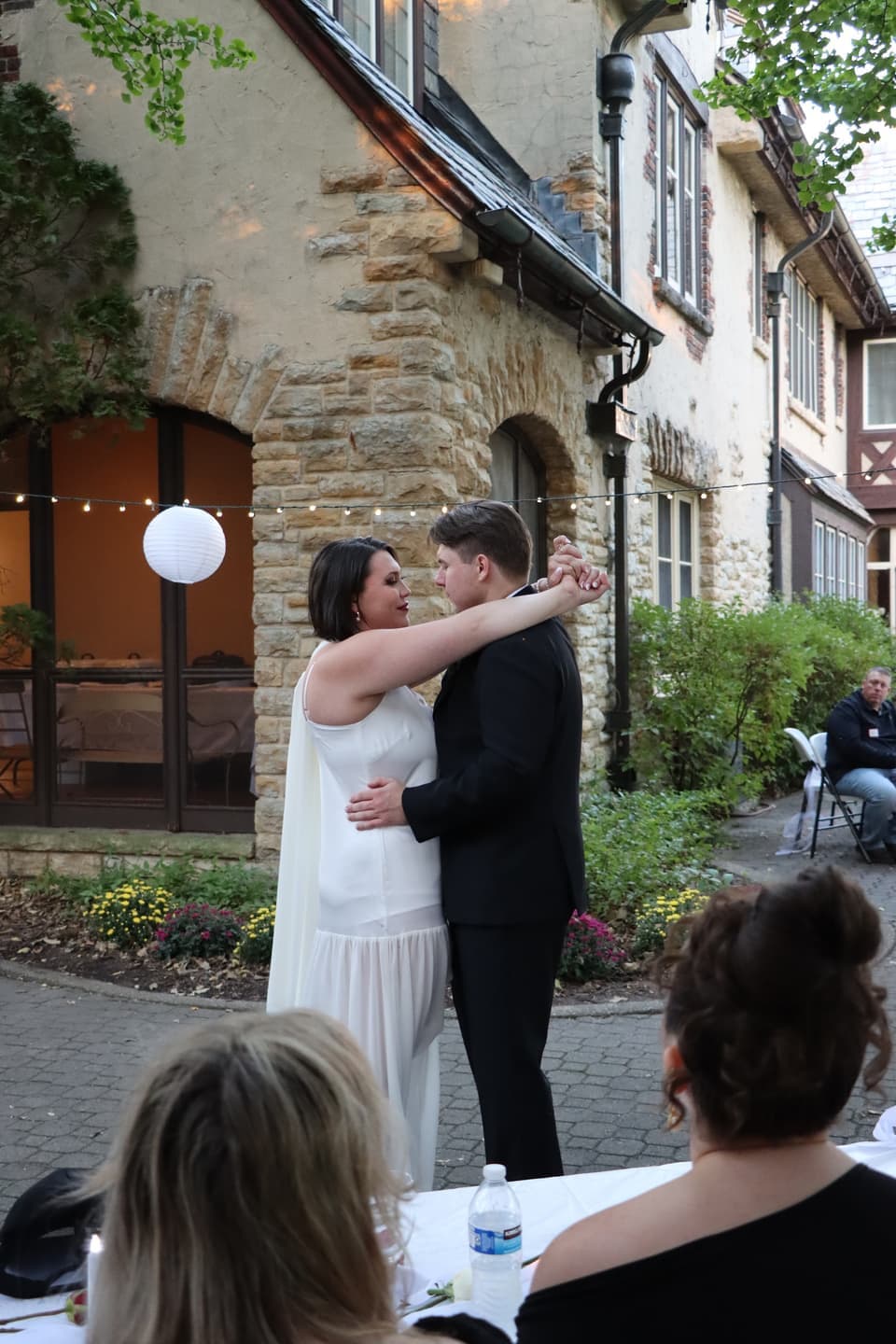 Abbi and Fred slow dance beside the house as guests watch