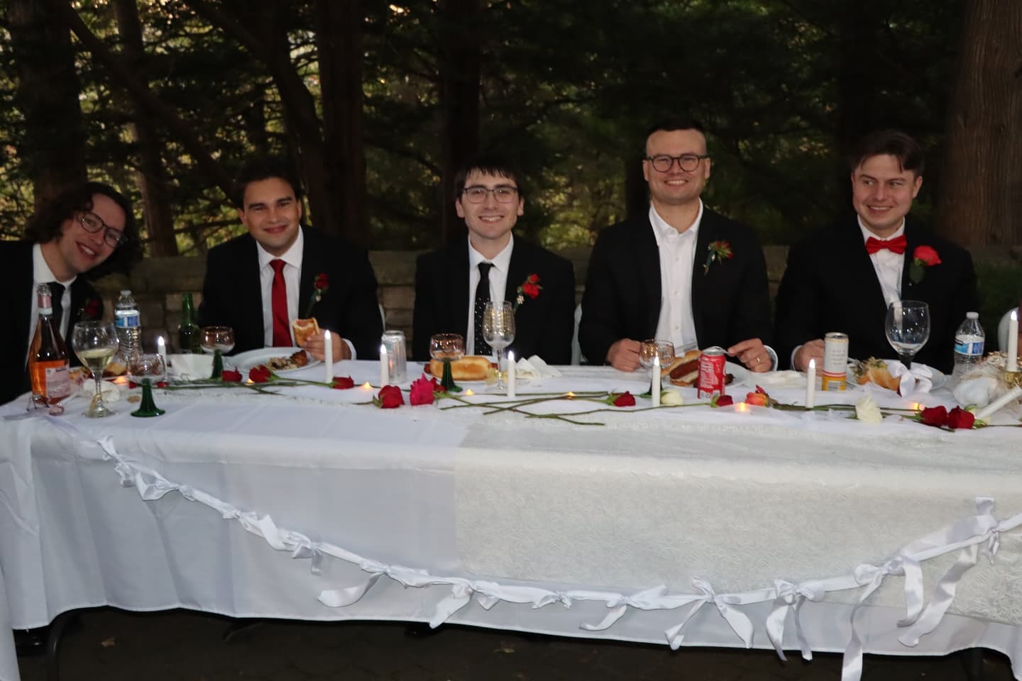 The groom's side of the head table in suits and red bow ties